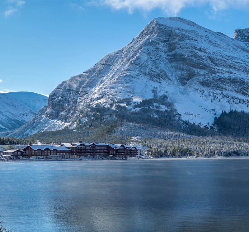 Large snow-covered mountain overlooking a lake with a lakeside lodge and forest in Montana